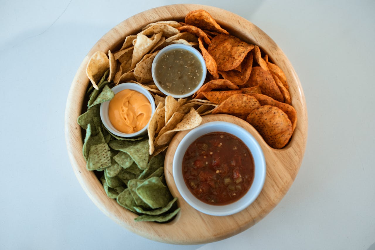 A vibrant assortment of nachos with salsas and cheese dip on a wooden platter.